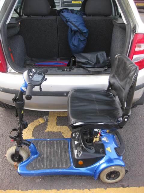 A mobility scooter positioned behind a car with its boot open, showing accessible transport options in Swindon.