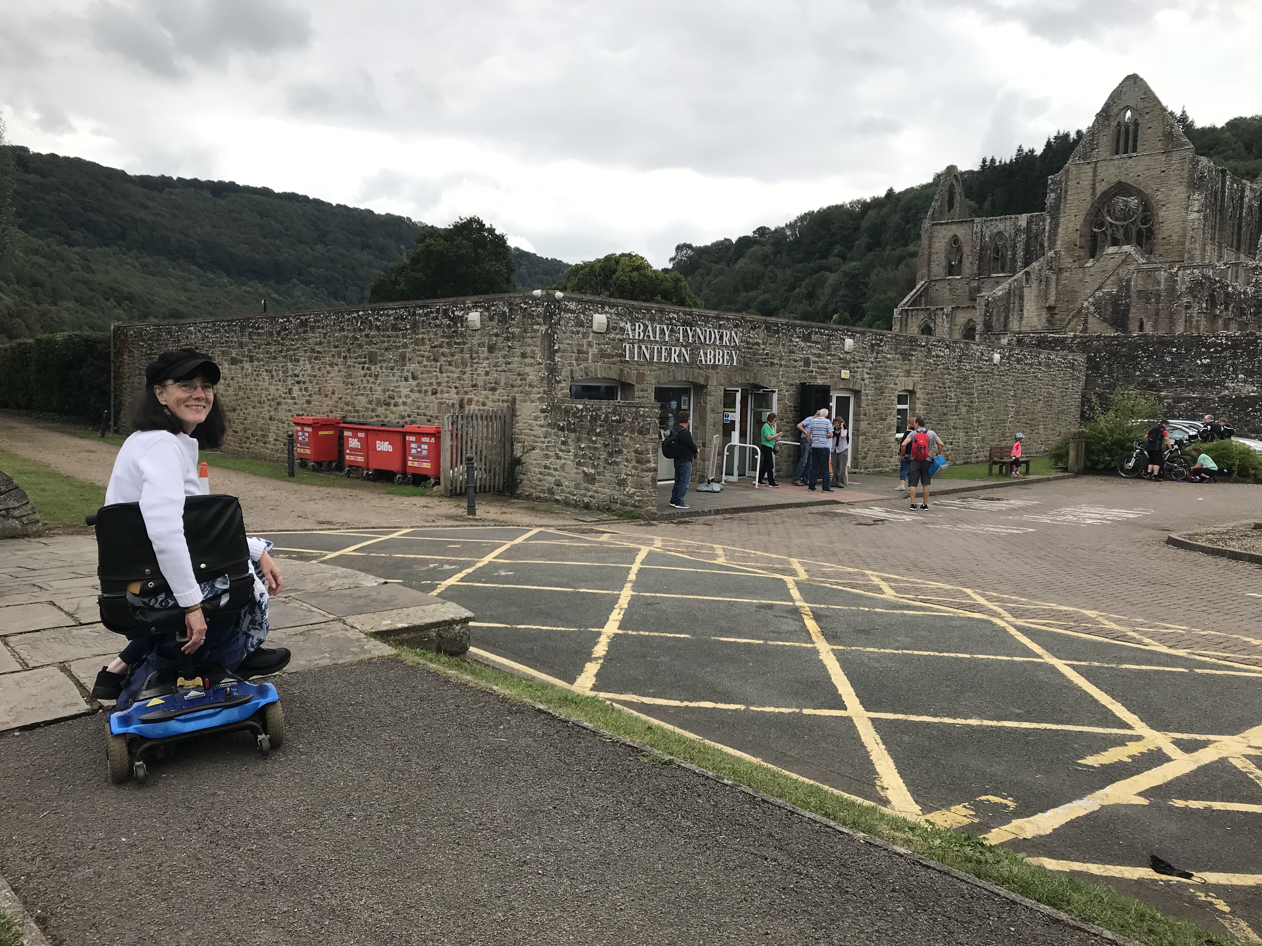 Wheelchair access at Tintern Abbey, showing writer, Katherine Owen, visiting from Swindon. A visitor using a mobility scooter at Tintern Abbey, with the abbey ruins and wheelchair accessible visitor centre in the background.